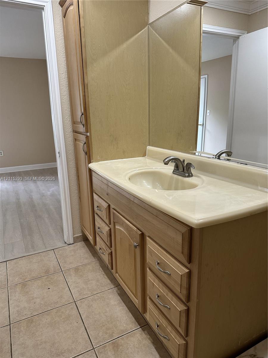 Vanity featuring light wood cabinetry, integrated storage tower, stone-composite countertop with molded sink, and a large-format vanity mirror with tile flooring
