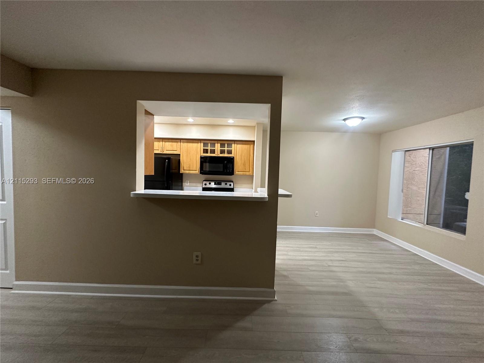 Interior space featuring wood-finish flooring, a pass-through kitchen window with a breakfast bar, recessed ceiling lighting, and a large sliding glass door