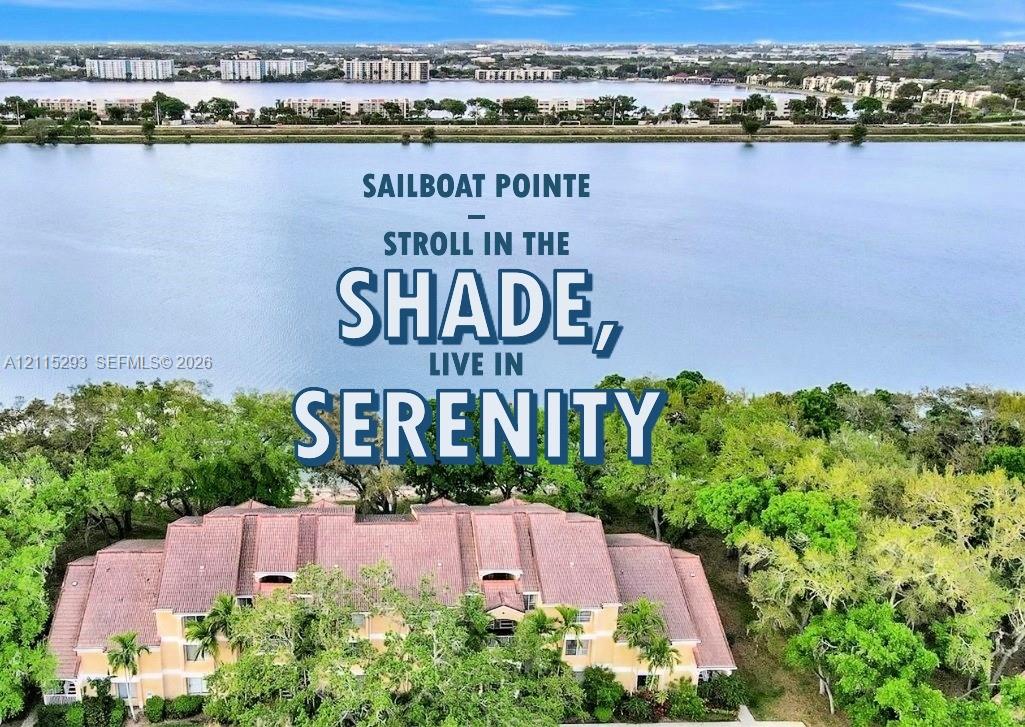 Aerial perspective of a multi-story residential building featuring a multi-gabled roof, light-toned exterior facade, and mature perimeter landscaping, situated directly along the shoreline of a large lake
