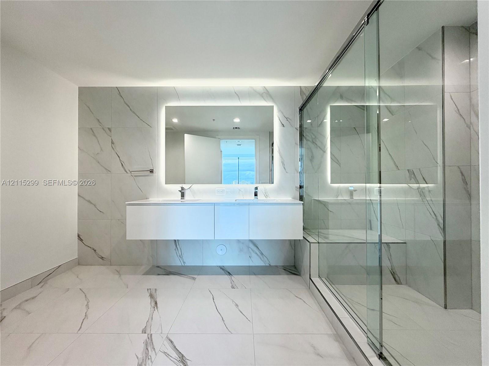 Floating dual-vanity with integrated sinks, back-lit mirror, wall-to-wall large-format tile, and glass-enclosed shower