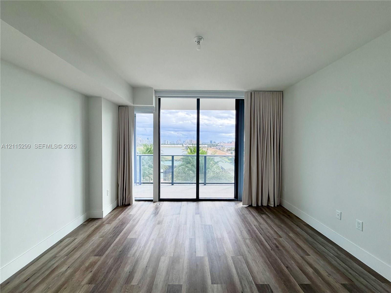 Wood-finish flooring, full-height sliding glass doors, and a private balcony with metallic railing