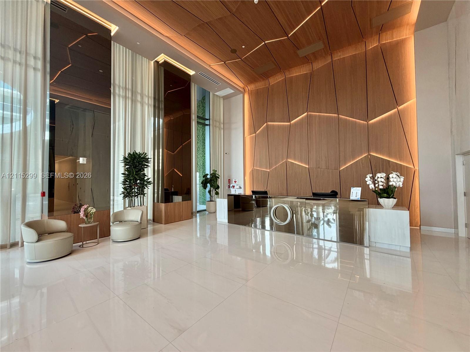 Grand lobby featuring expansive floor-to-ceiling windows, high-gloss stone tile flooring, custom wood-paneled feature wall with integrated accent lighting, and a mirrored reception desk