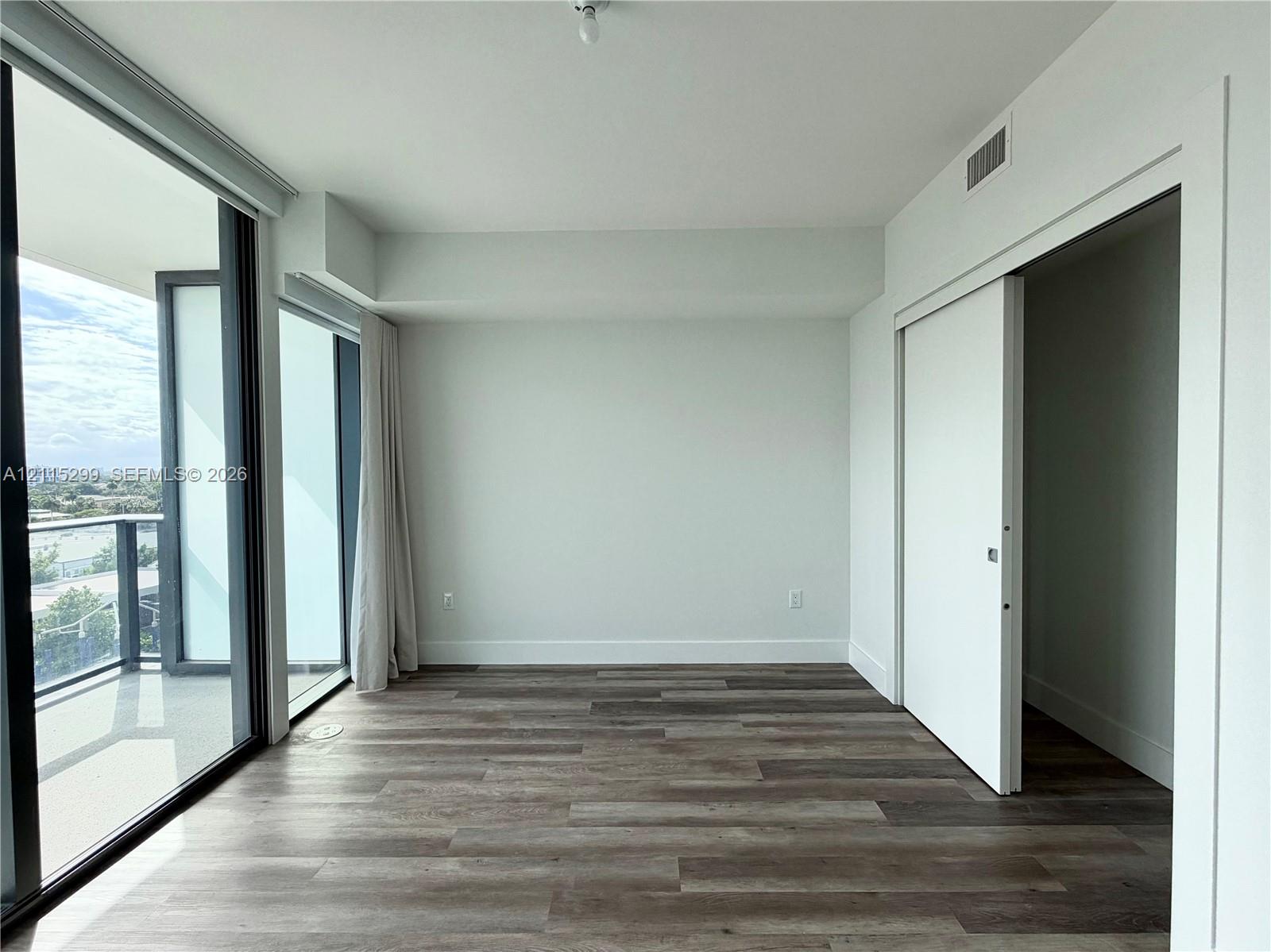 Interior space featuring wood-finish flooring, floor-to-ceiling glass paneling, a sliding door, and a balcony with a glass railing