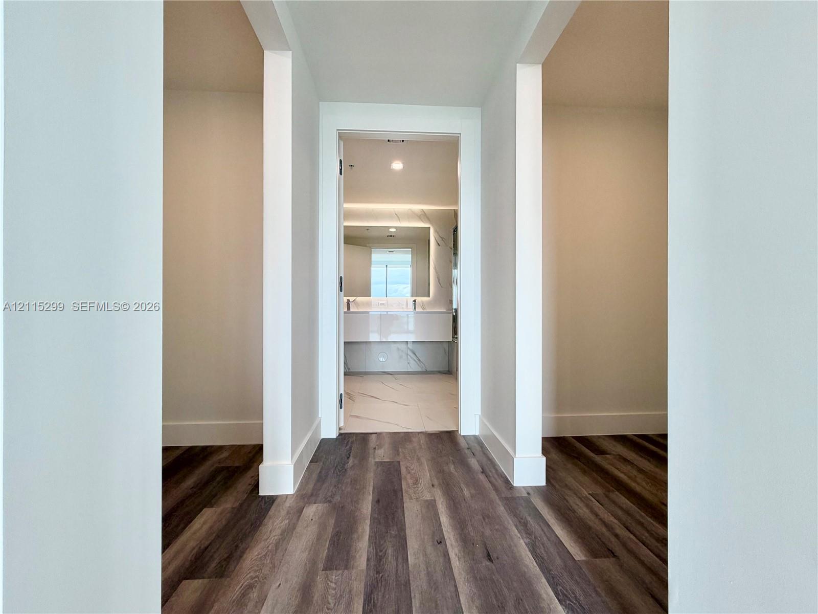 Wood-finish flooring, white walls, and a floating dual-sink vanity featuring stone-surround surfaces and a backlit mirror