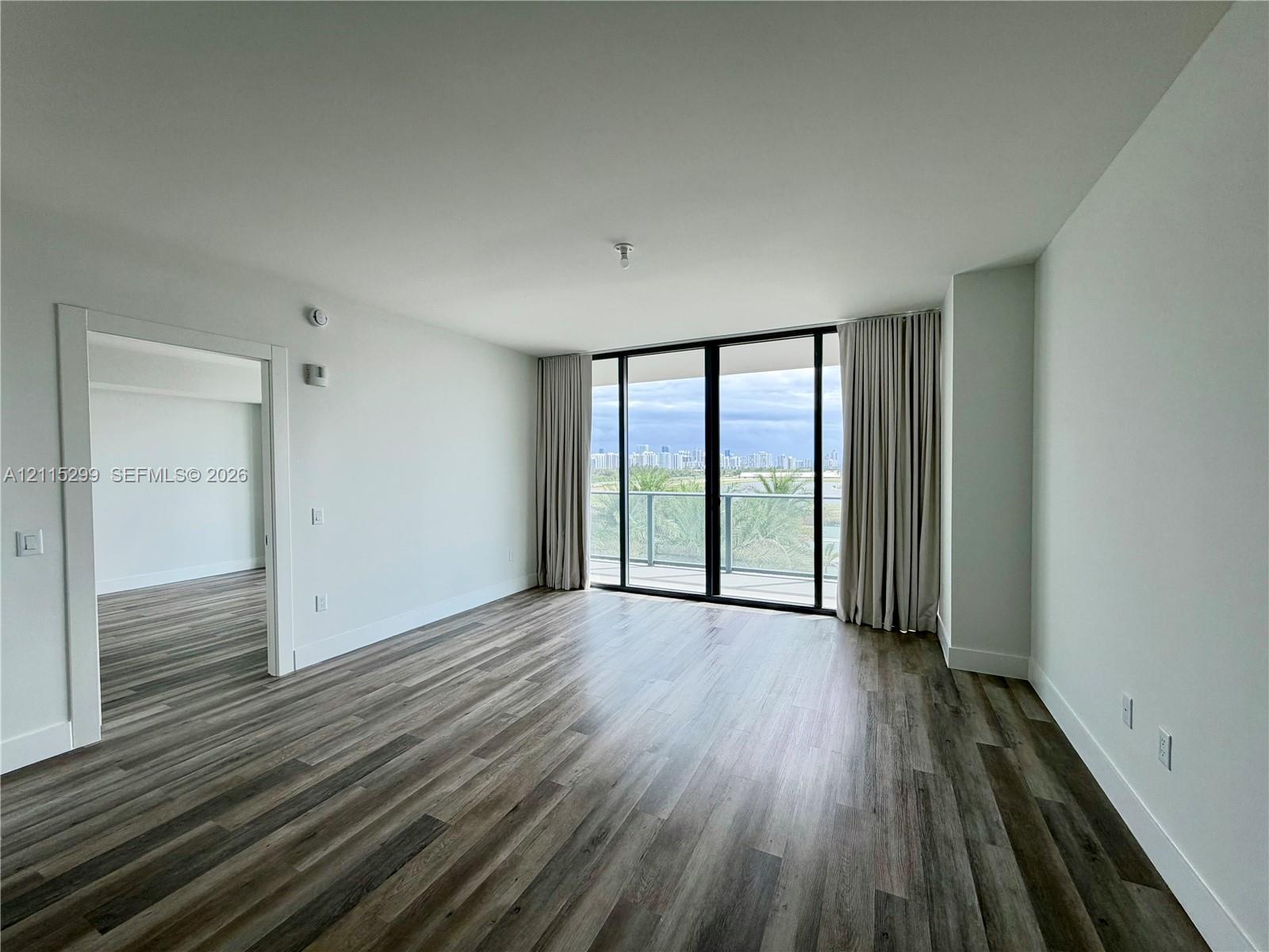 Open-concept room featuring wood-finish flooring, floor-to-ceiling glass sliding doors, and a private balcony