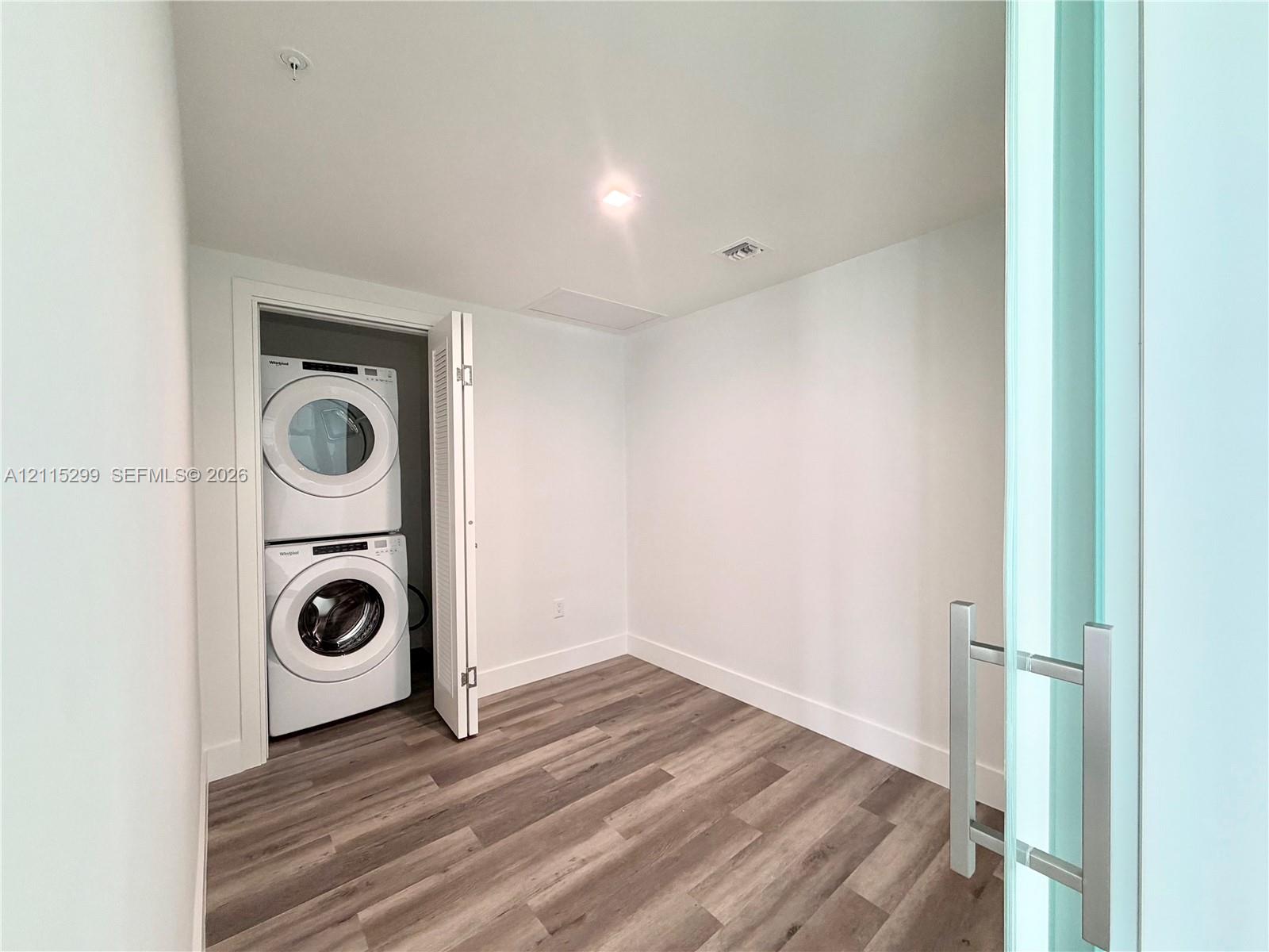 Stacked front-load washer and dryer set, wood-finish flooring, and sliding door with a metal handle