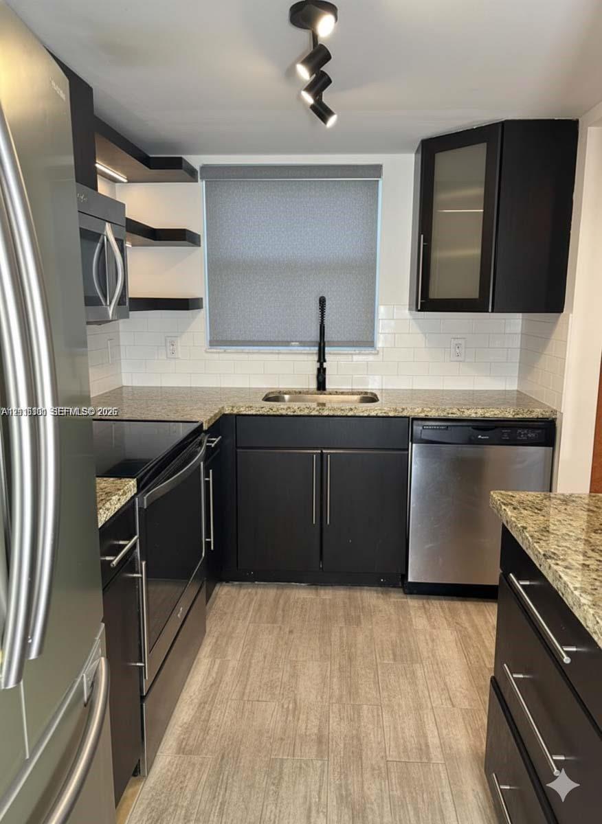 Kitchen featuring dark cabinetry, stone-finish countertops, stainless steel appliances, white subway tile backsplash, and wood-finish flooring