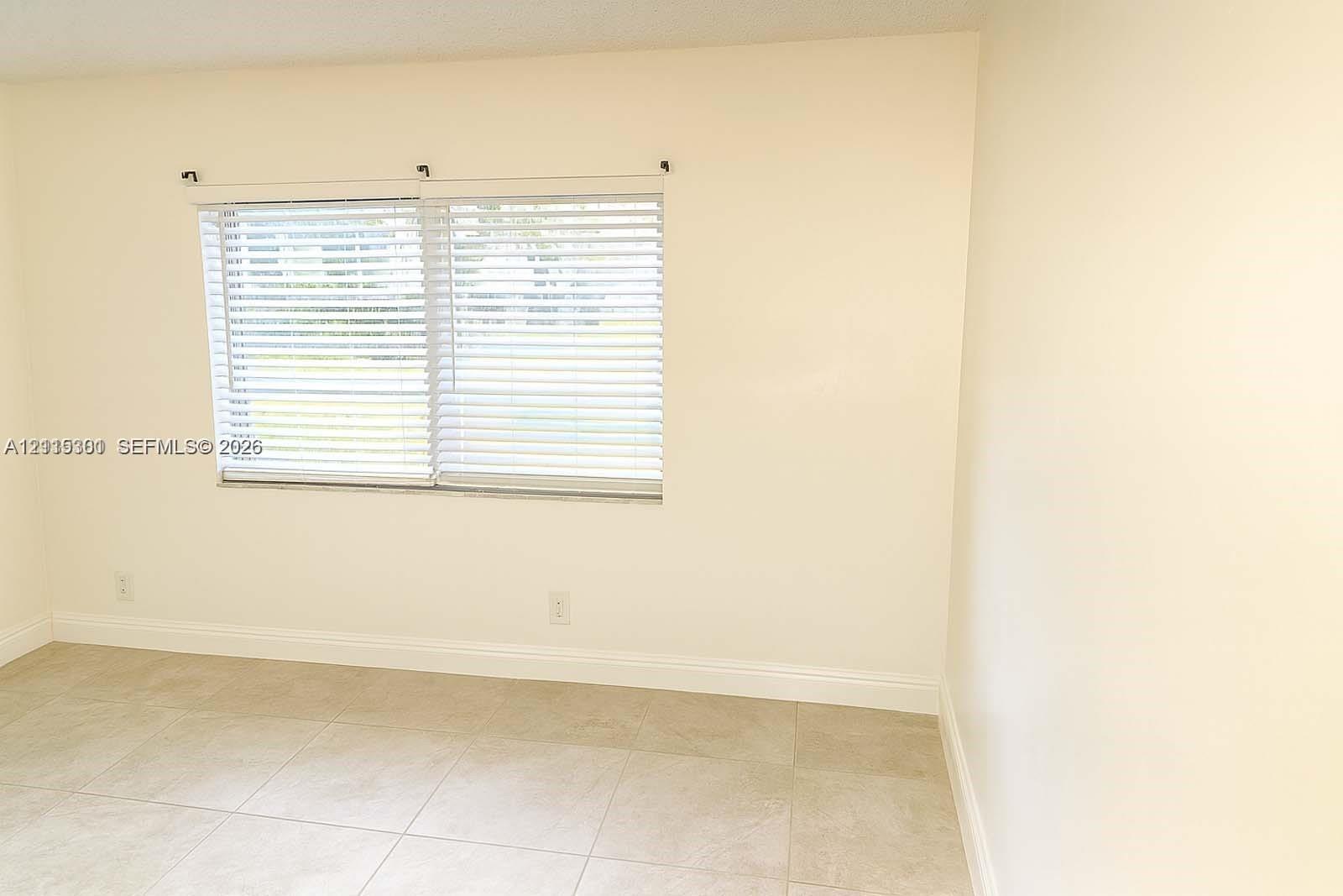 Neutral-toned interior space featuring light-colored tile flooring, smooth walls, and horizontal slat window blinds