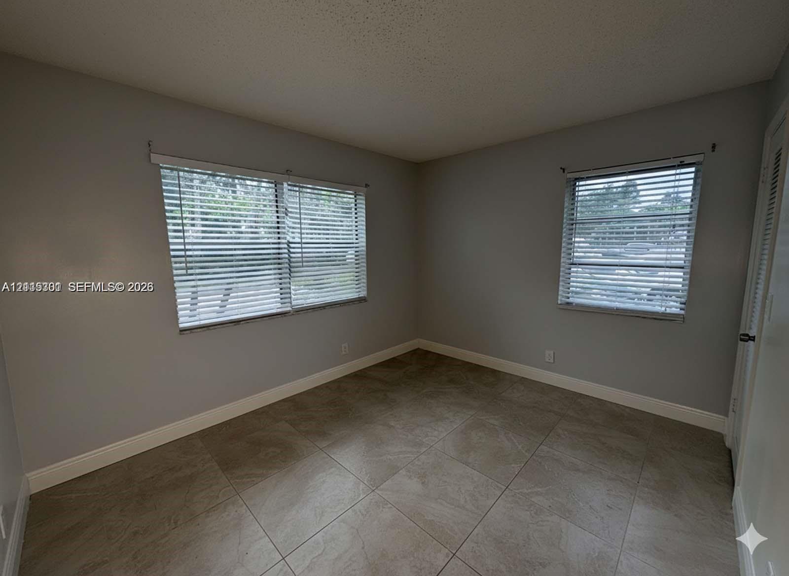 Neutral-toned interior featuring large-format tile flooring, dual windows with fitted horizontal blinds, and a louvered closet door