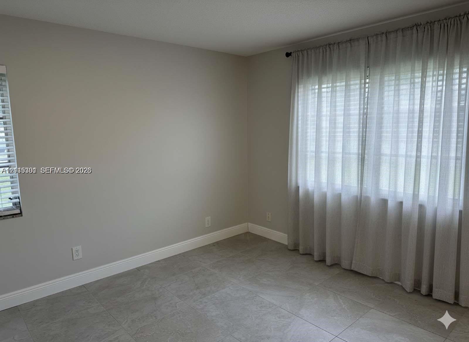 Neutral-toned interior space featuring large-format ceramic tile flooring, dual-aspect windows, and crisp wall finishes