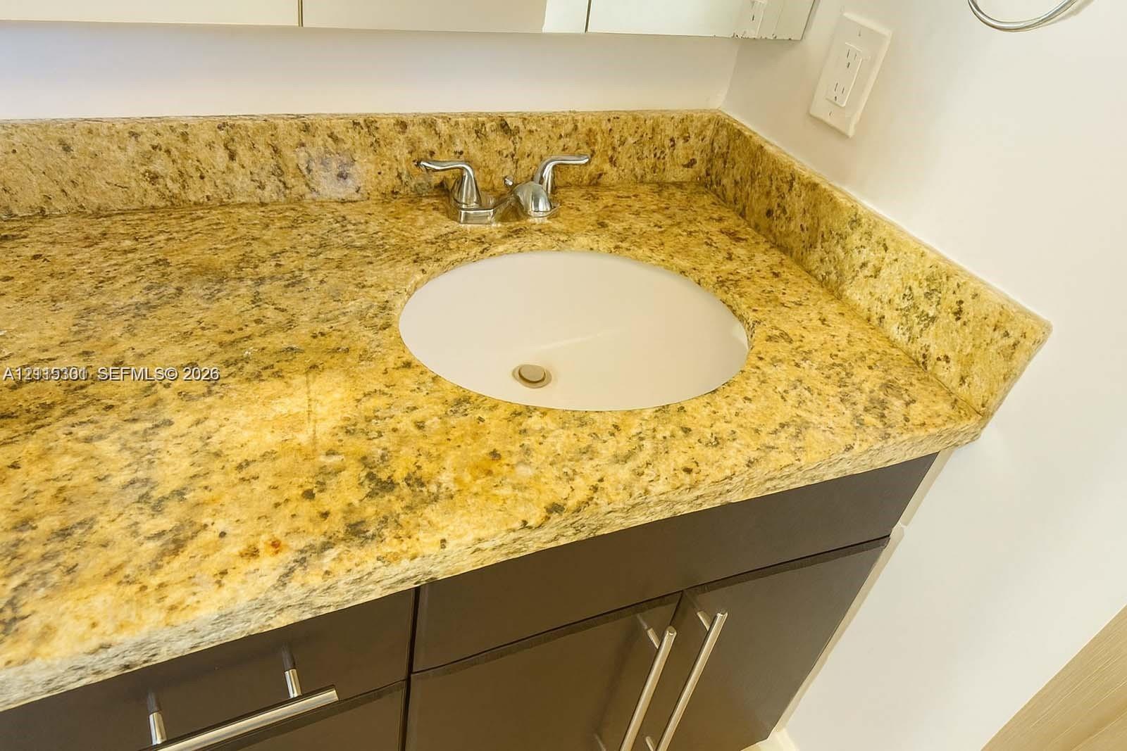 Vanity featuring a stone-composite countertop with an integrated undermount sink, chrome double-handle faucet, and dark-toned cabinetry with metallic hardware