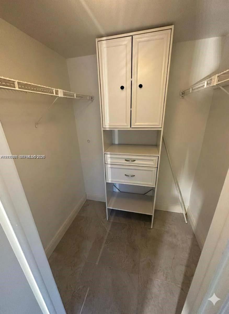 Walk-in closet featuring white built-in cabinetry with two drawers and two cabinet doors, dual-level wire shelving, and neutral tile flooring