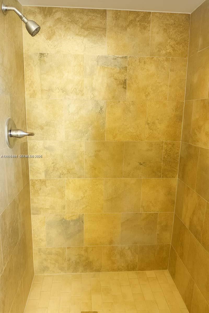 Walk-in shower featuring large-format textured stone wall tile, linear tile floor, and polished metal shower fixtures