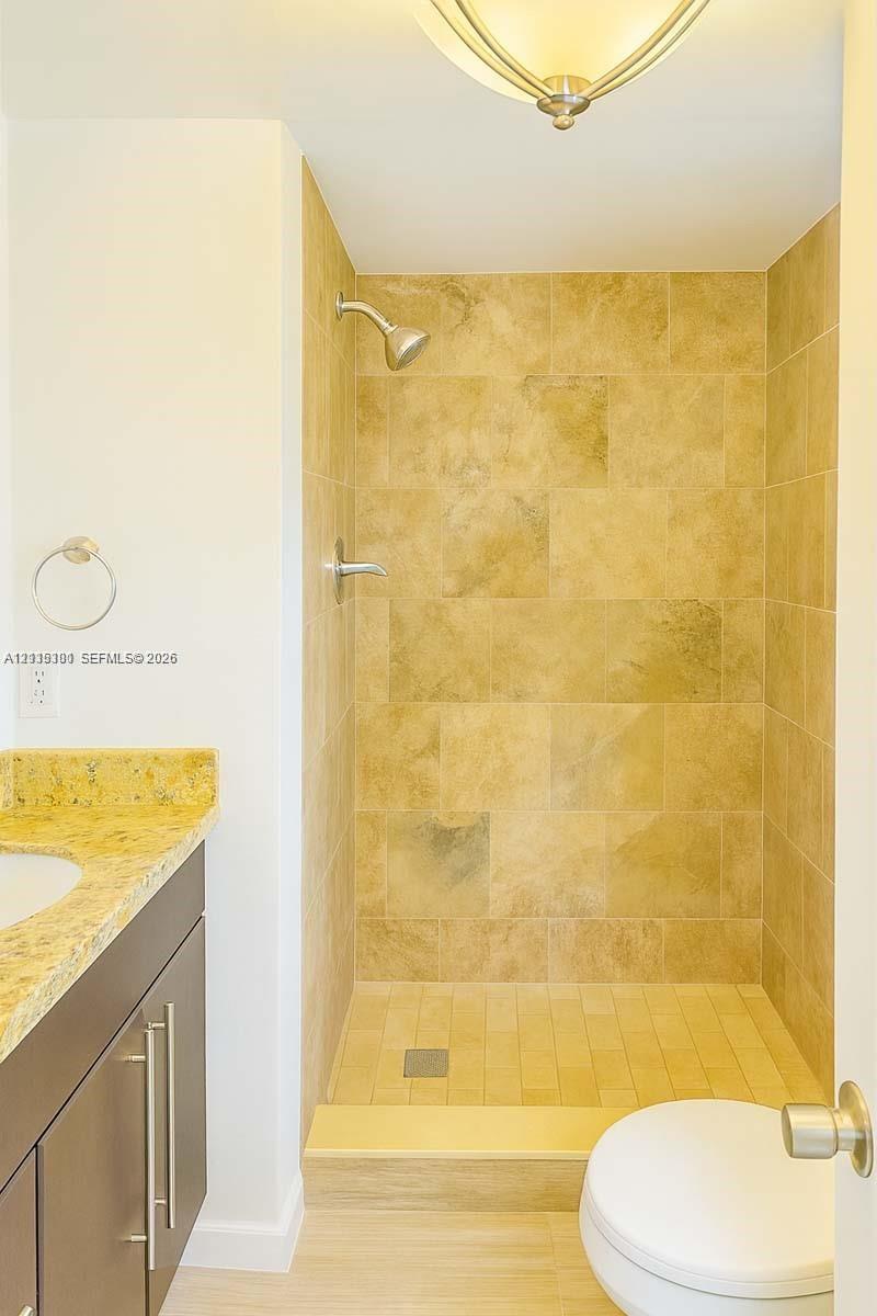 Walk-in shower with stone-tile surround, dark-finish cabinetry, stone countertop with integrated sink, and polished metal hardware