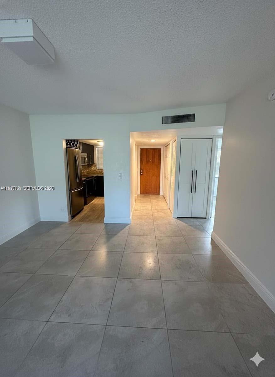 Large-format ceramic tile flooring, solid wood-finish entry door, built-in double-door closet cabinetry with vertical hardware, and flush-mount rectangular ceiling lighting