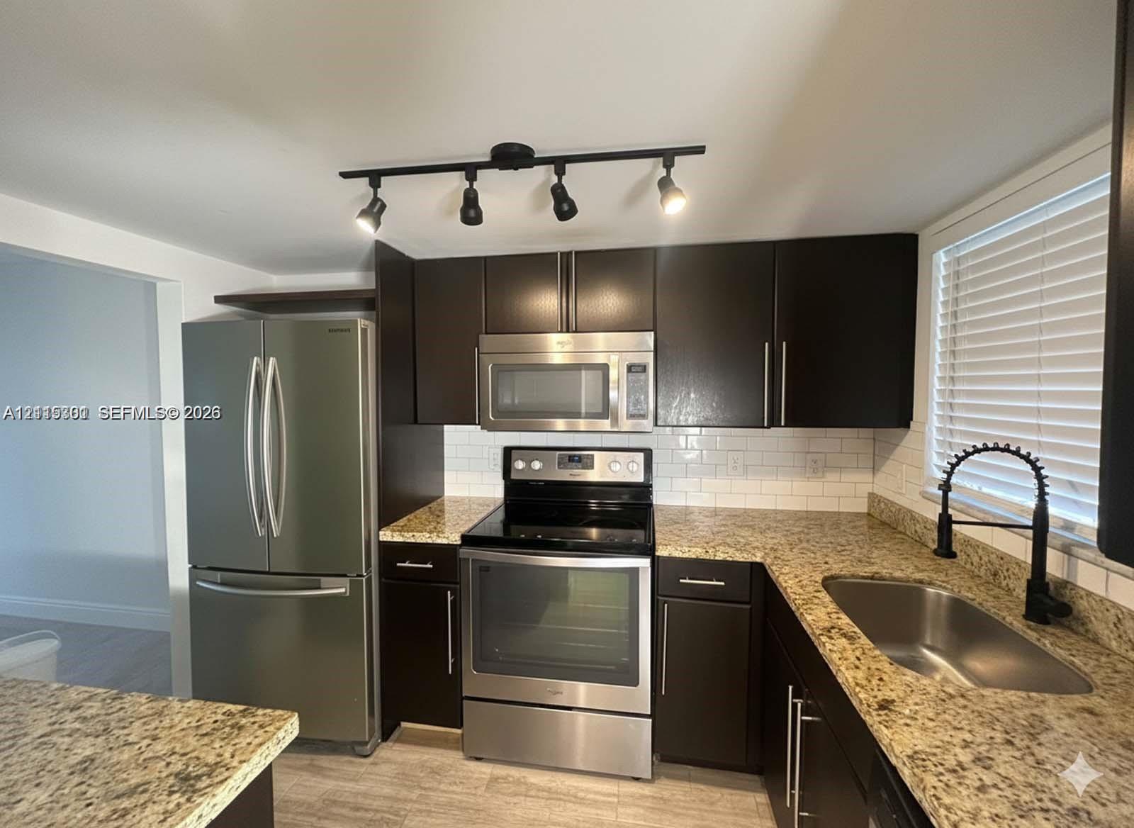 Kitchen featuring dark wood cabinetry, stainless steel appliances, stone countertops, a white subway tile backsplash, and a matte black gooseneck faucet