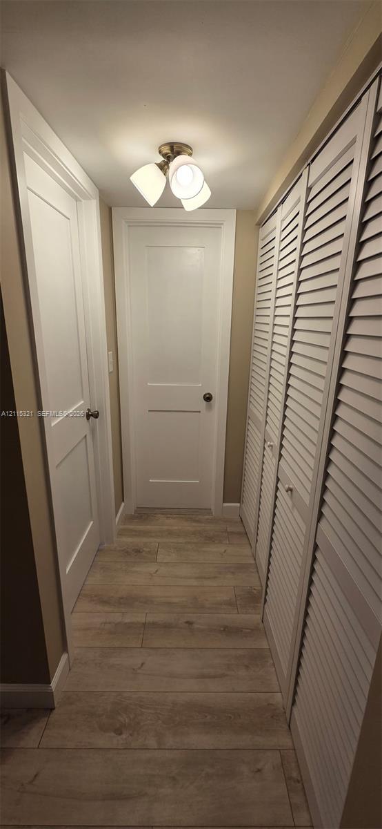 Interior corridor featuring wood-finish plank flooring, two-panel shaker-style doors, louvered closet doors, and a multi-light flush-mount ceiling fixture