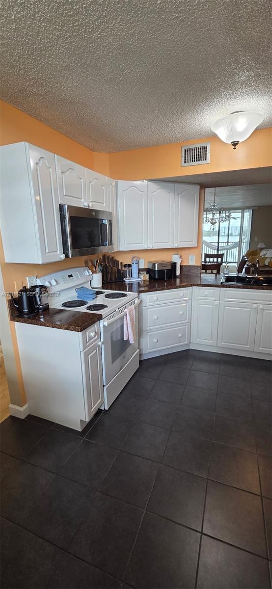 Kitchen featuring white shaker-style cabinetry, stone-finish countertops, dark tile flooring, and integrated stainless steel microwave