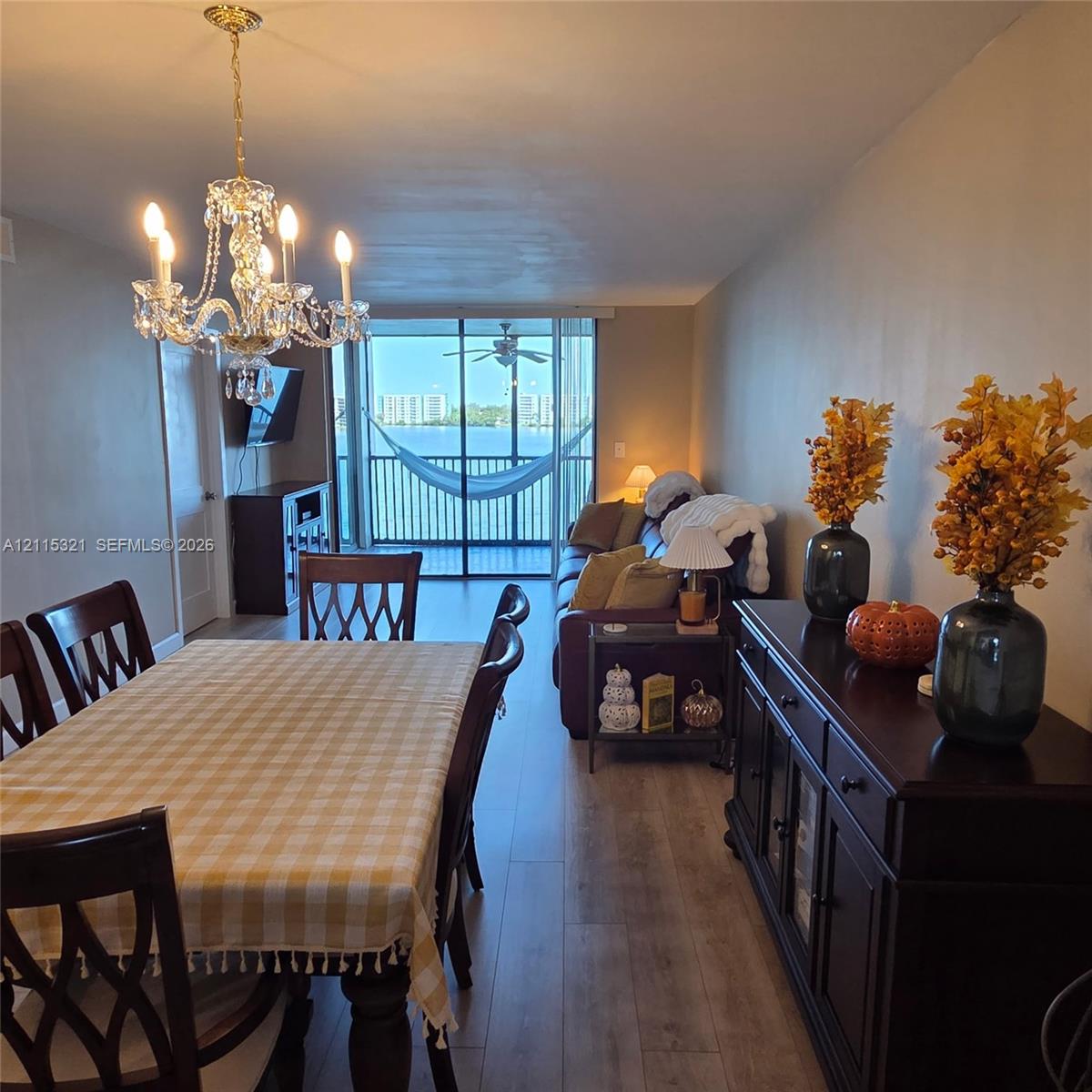 Open-concept interior featuring wood-finish flooring, a multi-arm crystal chandelier, and a screened-in balcony with water scenery