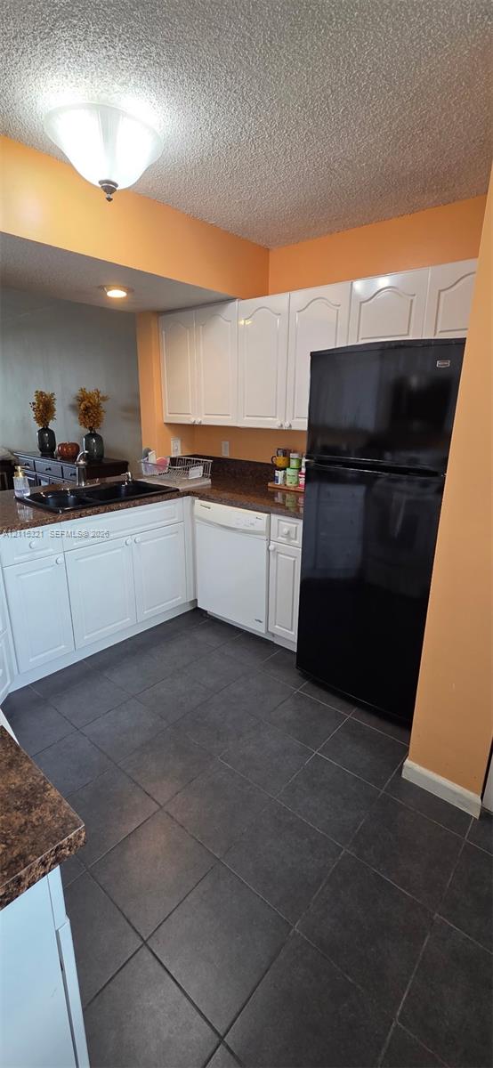 Kitchen featuring white cabinetry, dark stone-finish countertops, black-finish sink, large-format tile flooring, and integrated appliances
