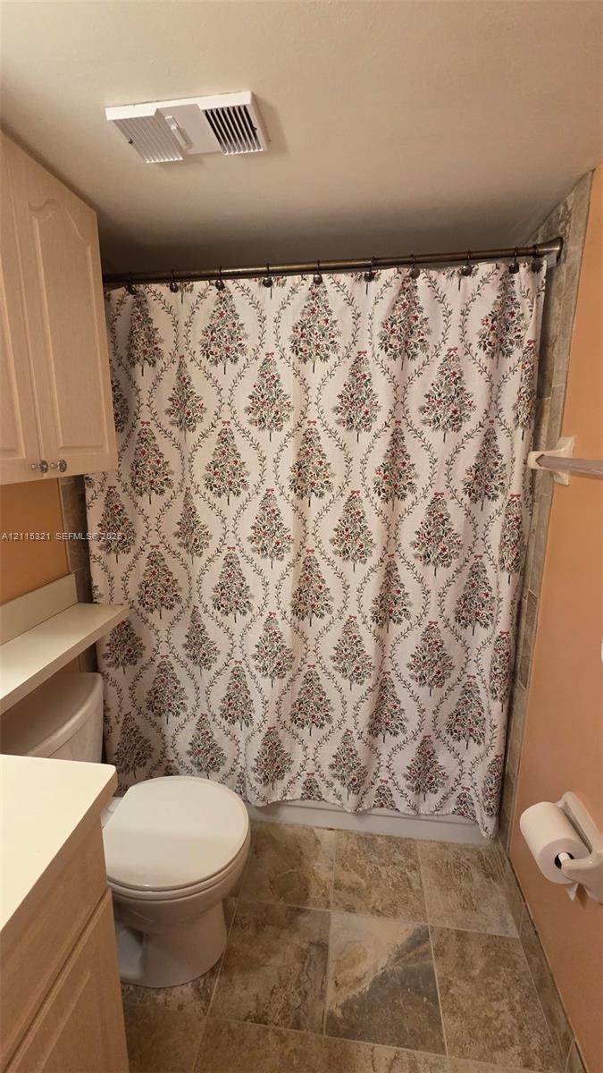 Bathroom featuring light-finish cabinetry, neutral solid-surface countertop, stone-finish tile flooring, and a wall-mounted towel bar