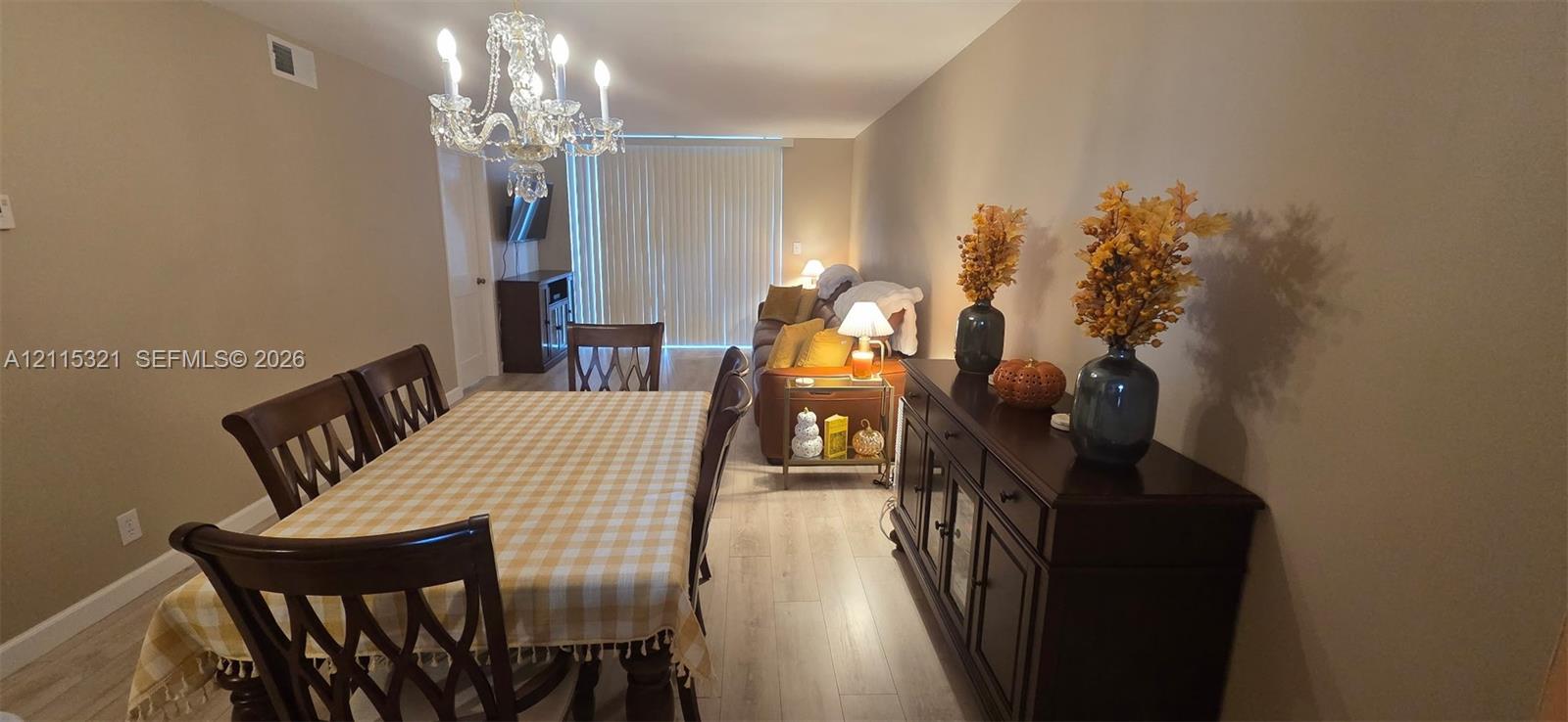 Light-toned wood-finish flooring, crystal chandelier, and sliding glass door with vertical blinds