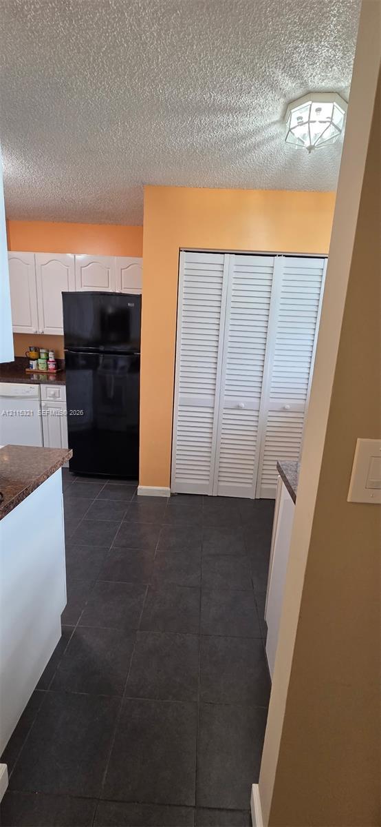 Kitchen featuring dark stone-finish countertops, white cabinetry, dark tile flooring, and white louvered bifold closet doors