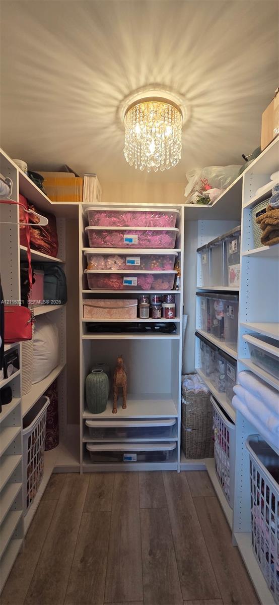 Custom walk-in closet featuring white built-in cabinetry, tiered shelving, integrated pull-out drawers, wood-finish flooring, and a decorative crystal flush-mount light fixture
