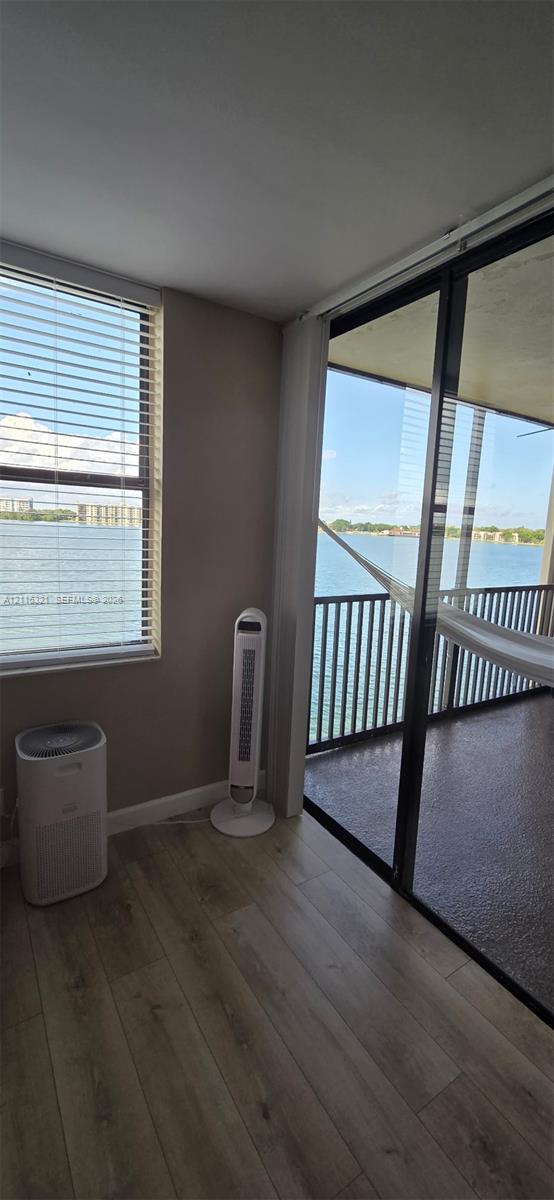 Wood-finish flooring, floor-to-ceiling windows, sliding glass door, and covered balcony with metal railing overlooking the water