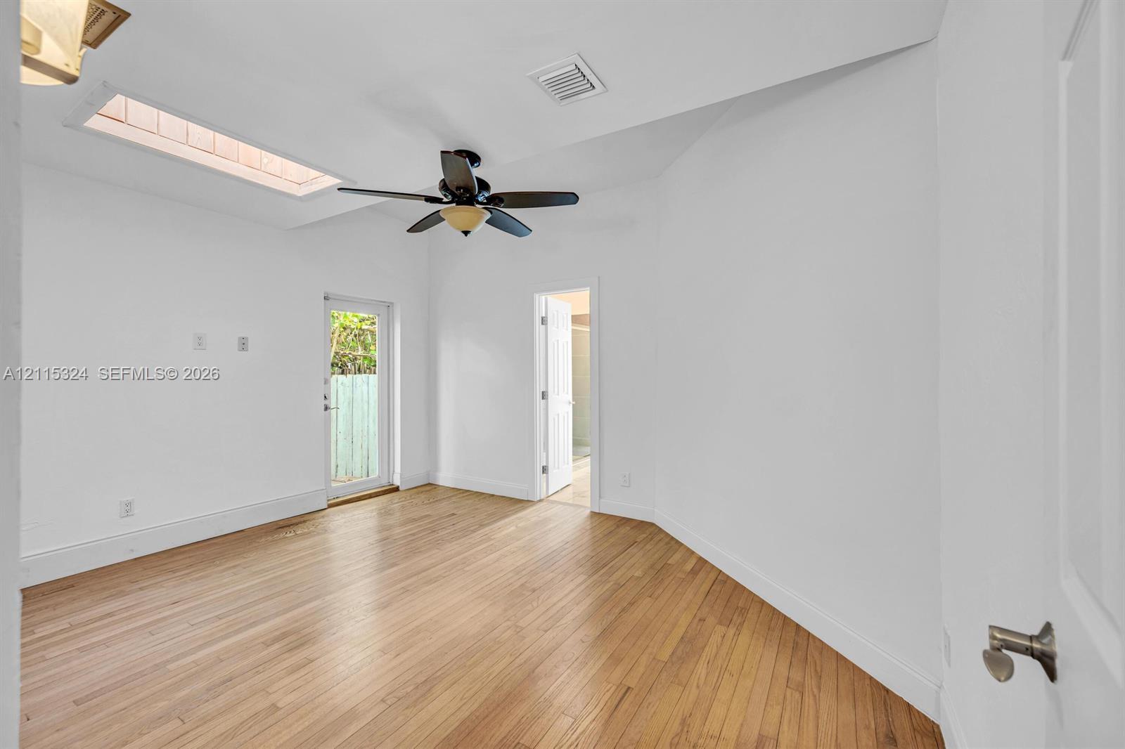Interior space featuring wood-finish flooring, a vaulted ceiling with a skylight, a ceiling fan with integrated lighting, and an exterior glass-panel door