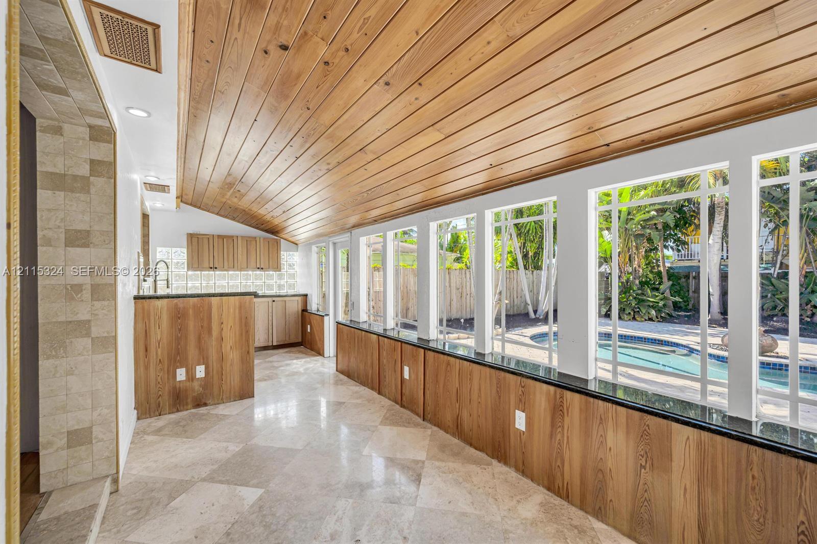 Vaulted wood-plank ceiling, stone tile flooring, built-in wooden cabinetry, custom millwork wall paneling with integrated stone countertops, and extensive floor-to-ceiling windows