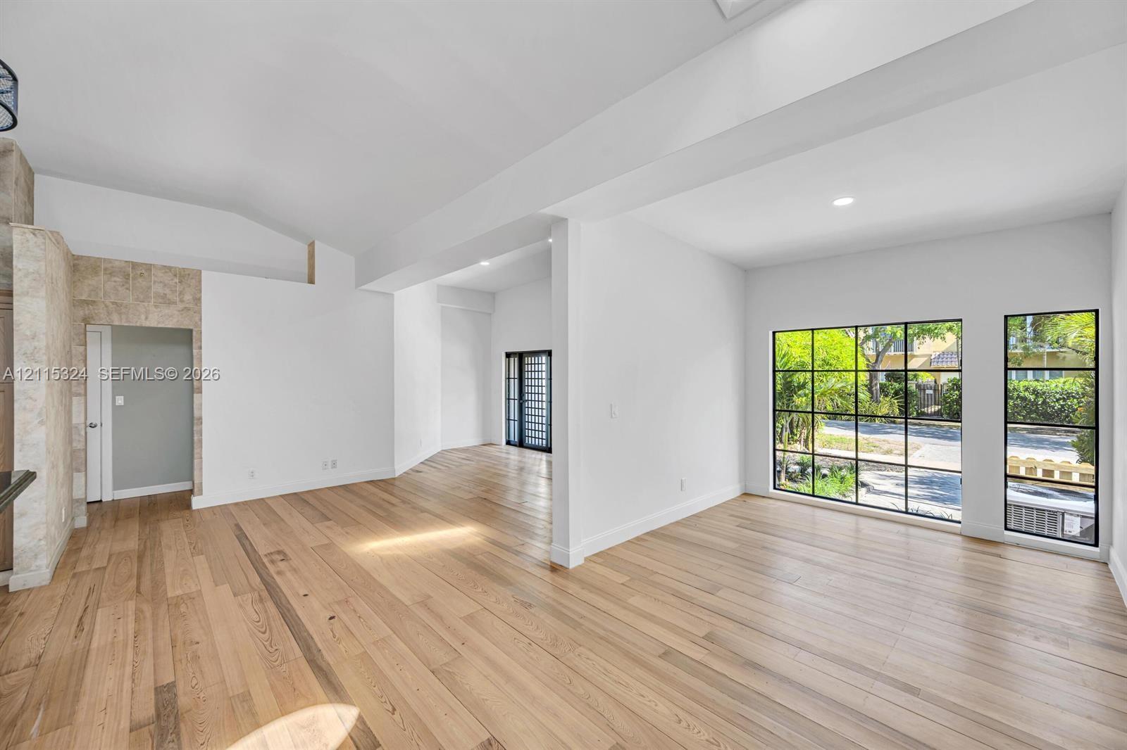 Interior featuring vaulted ceilings, wide-plank wood-finish flooring, floor-to-ceiling grid-style windows, and stone-surround wall accents