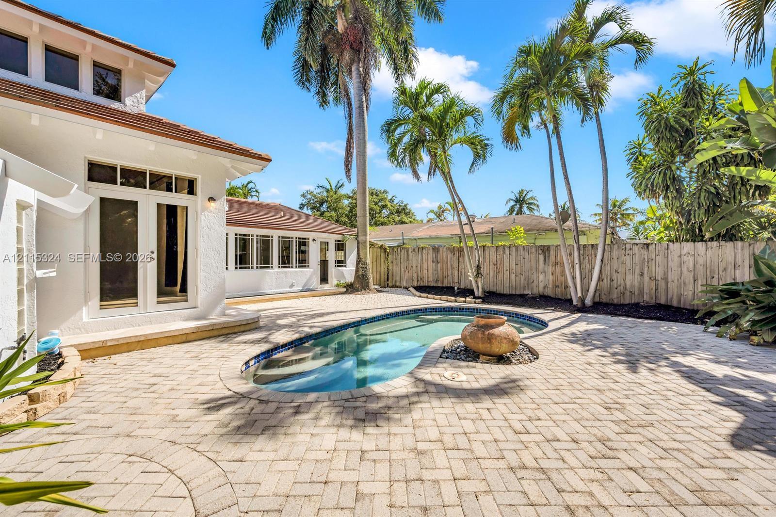 Backyard featuring a paver patio, in-ground pool with a decorative stone water feature, mature palm trees, and wood-style privacy fencing