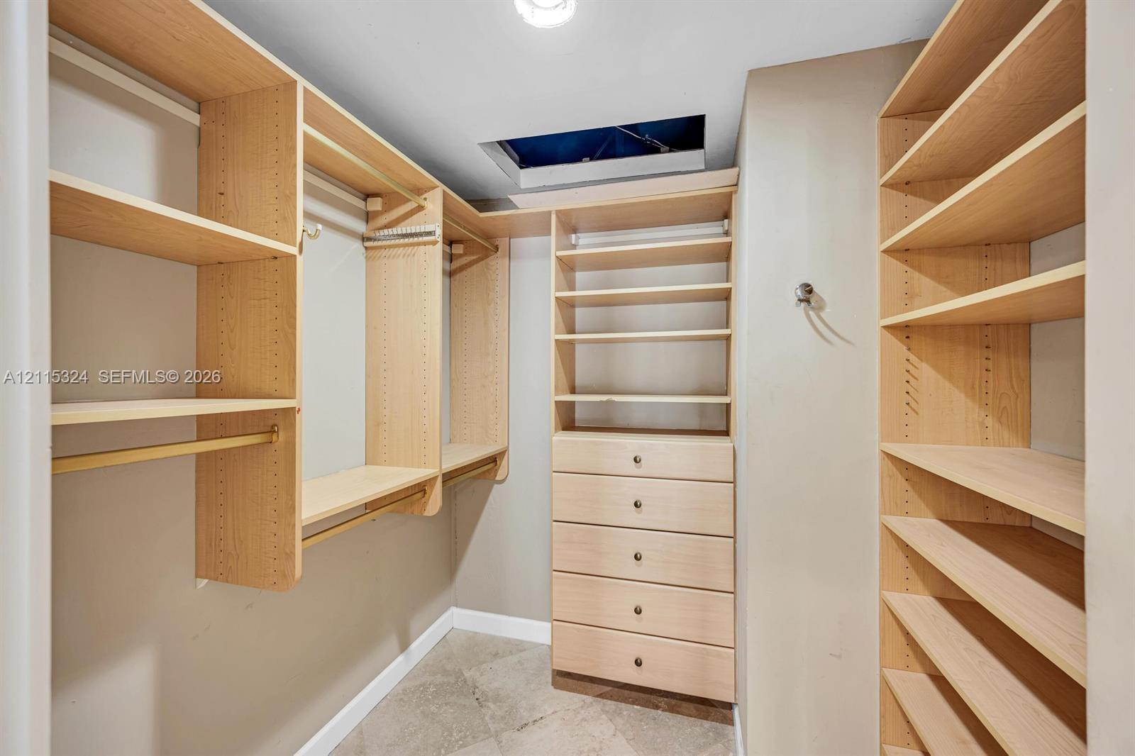 Walk-in closet featuring light wood-finish built-in cabinetry, floor-to-ceiling adjustable shelving, integrated garment rods, and five soft-close drawers with metallic hardware