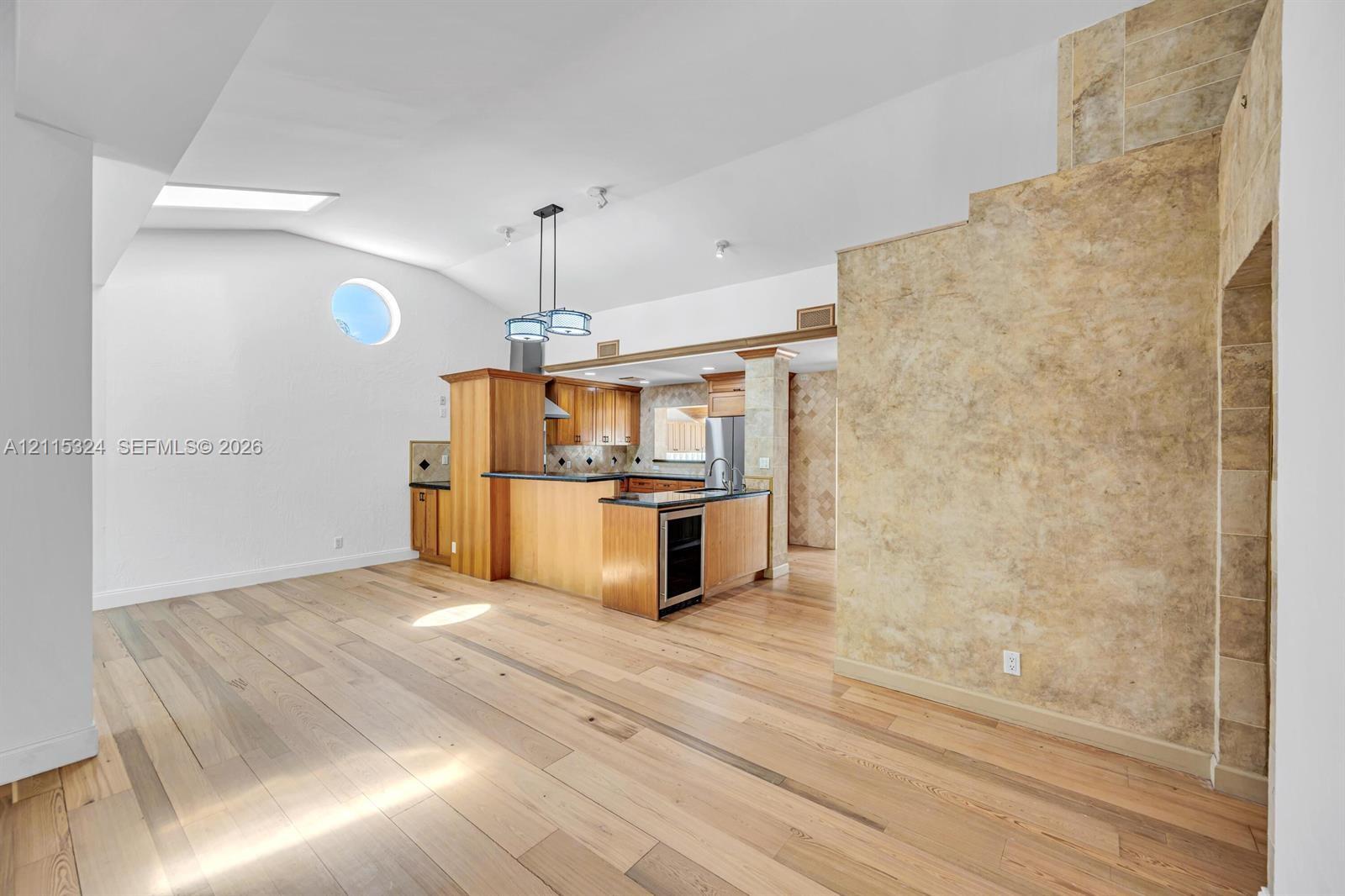 Vaulted ceilings featuring a skylight and circular window, wide-plank wood-finish flooring, full-height stone-finish accent wall, and cabinetry with integrated appliances