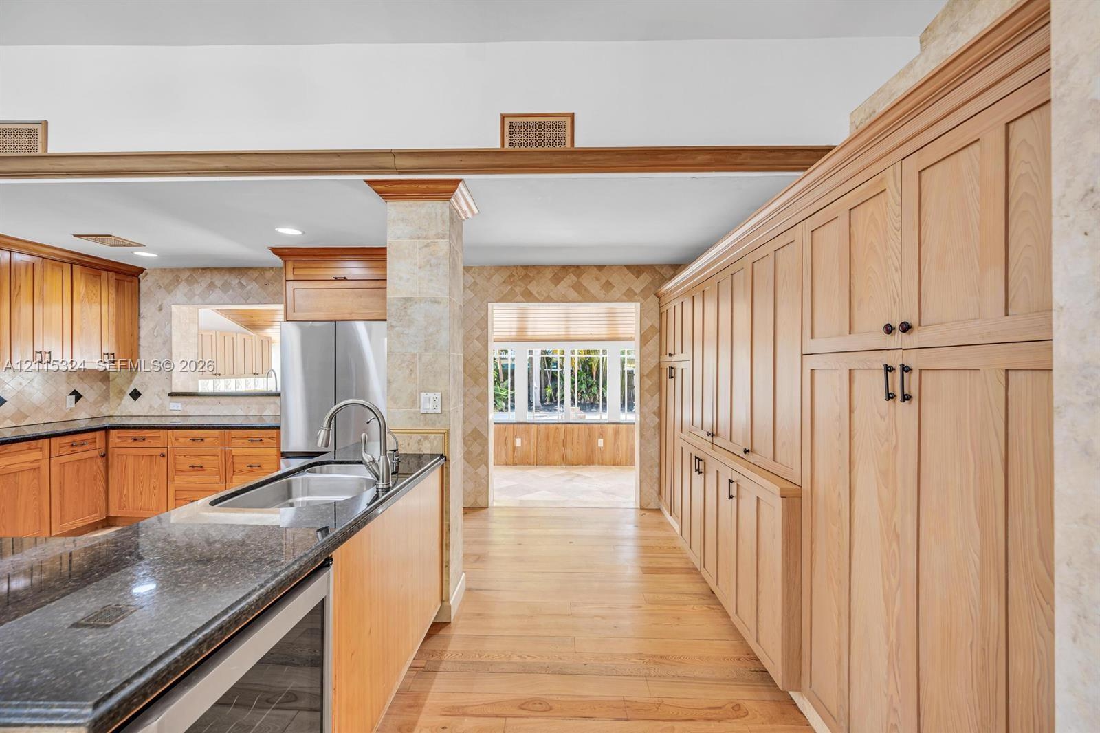 Custom cabinetry featuring wood-finish lower and full-height built-in storage, dark stone countertops, stainless steel undermount sink, and herringbone tile backsplashes