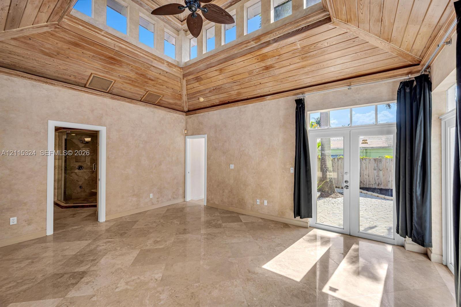 High-ceiling room featuring a wood-plank tray ceiling, clerestory windows, natural stone tile flooring, and French doors