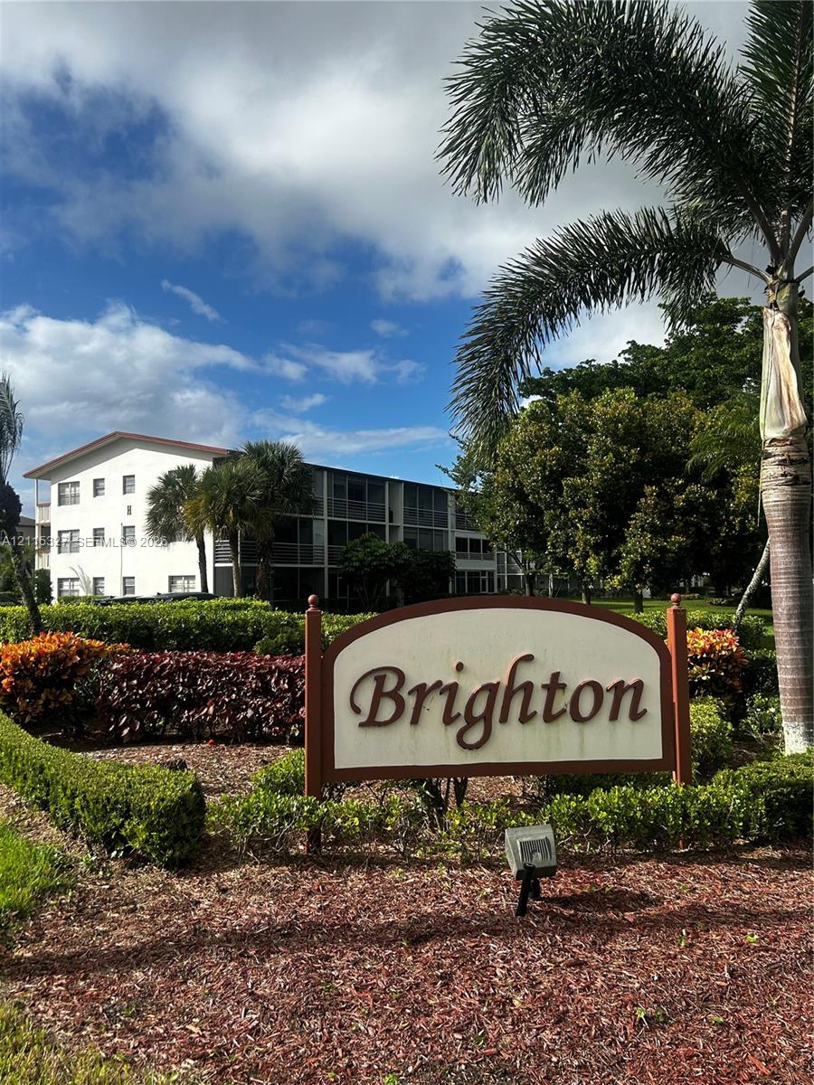 Property entrance signage featuring a painted wooden monument sign, complemented by landscaped garden beds, manicured shrubs, and mature palm trees