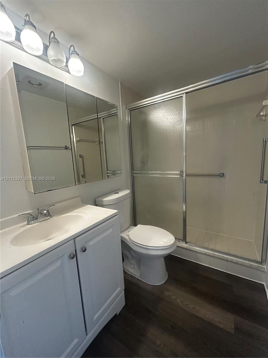 Bathroom featuring a vanity with integrated sink, tri-fold mirrored medicine cabinet, four-light vanity fixture, enclosed walk-in shower, and dark wood-finish flooring
