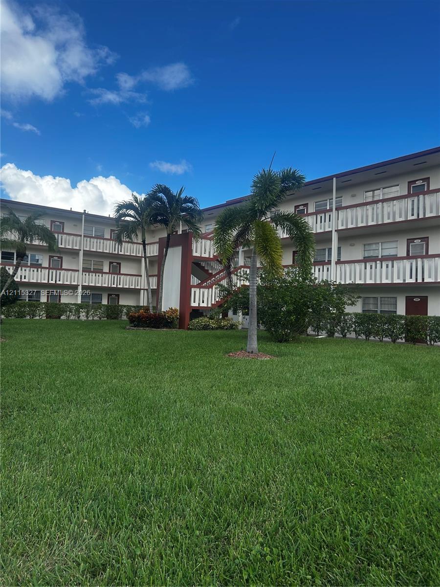 Multi-story exterior featuring white balconies, dark-framed sliding windows, integrated staircases, and surrounding palm trees