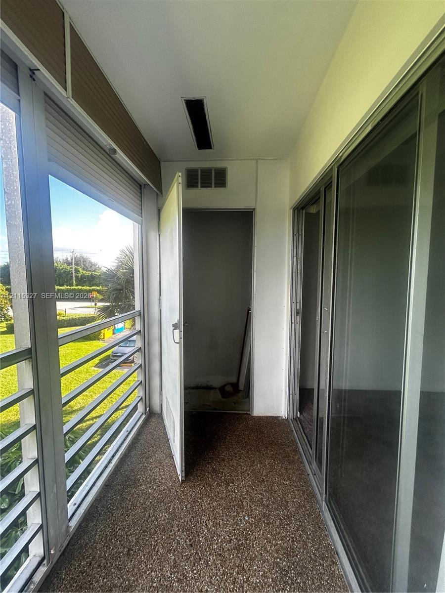 Enclosed balcony featuring a pebble-finish floor, floor-to-ceiling metal-framed windows, and a swinging utility door