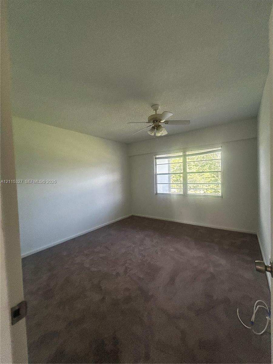 Neutral-toned carpeting, ceiling-mounted light fixture with fan, and horizontal window blinds