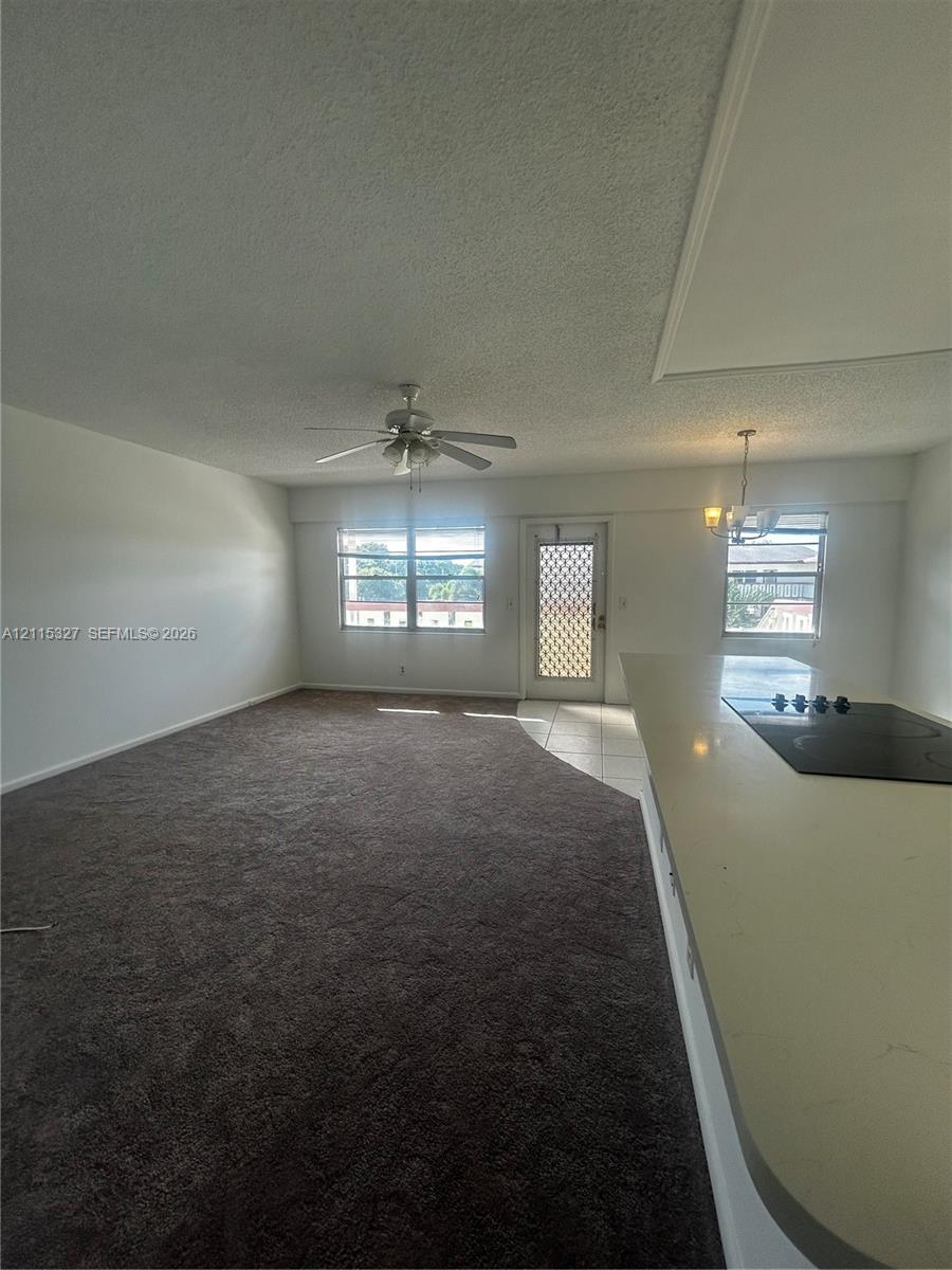 Open-concept interior featuring wall-to-wall carpeting, a kitchen island with a cooktop, a ceiling fan, and multi-pane windows