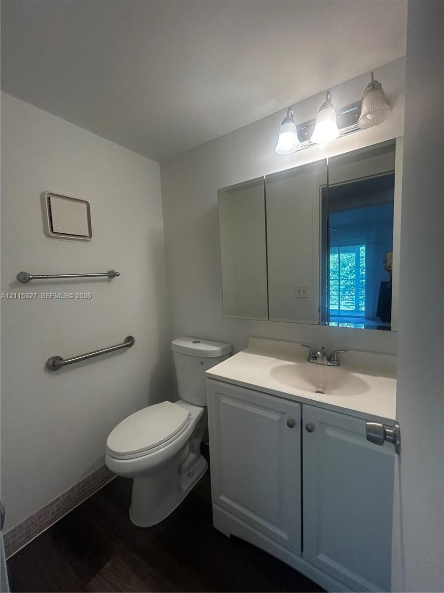 Bathroom featuring a white vanity cabinet with an integrated sink, tri-panel mirrored medicine cabinet, three-light wall fixture, and wood-finish flooring
