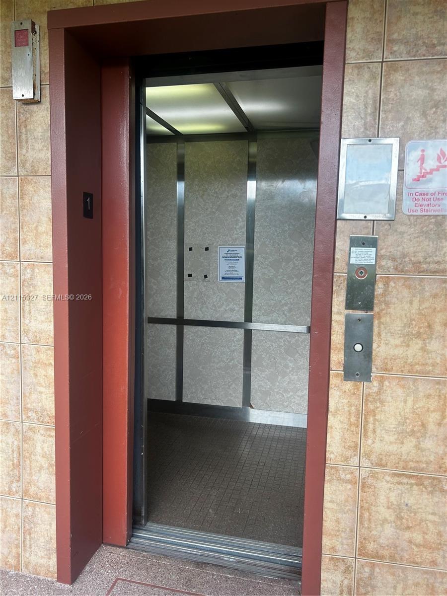 Elevator featuring brushed metal interior panels, integrated ceiling lighting, and tile-surround entry