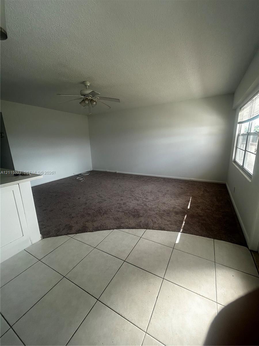 Spacious interior featuring large-format tile flooring, plush wall-to-wall carpeting, ceiling fan with light fixture, and large paneled windows