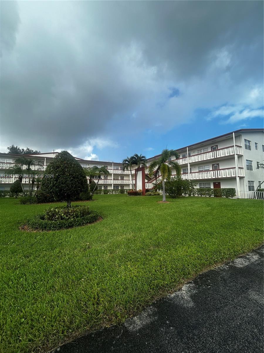 Multi-story building featuring wrap-around railed balconies, expansive green lawn, and mature palm trees