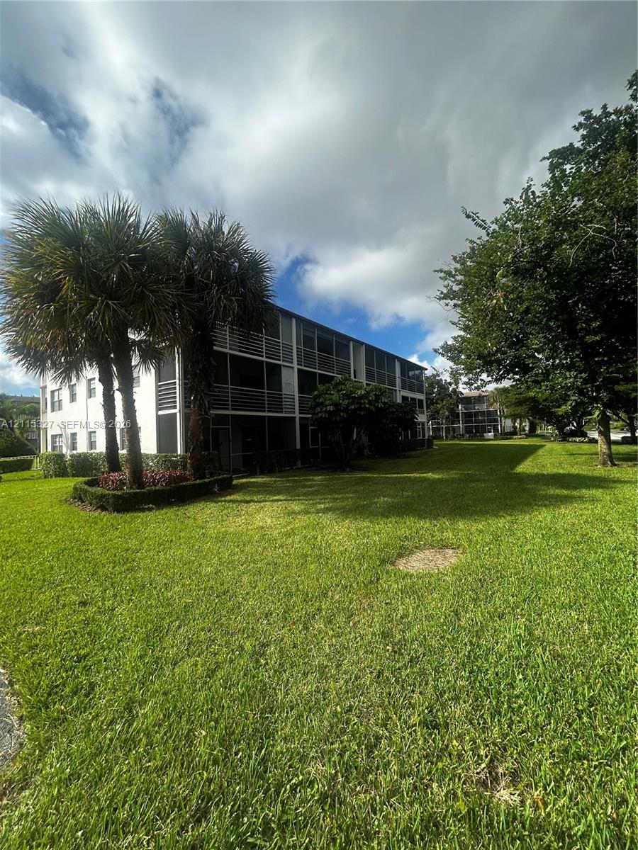 Multi-story exterior with screened balconies, expansive lawn, and mature landscaping