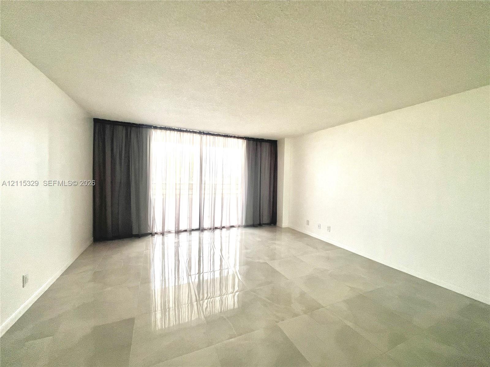 Spacious interior featuring large-format polished tile flooring, neutral wall finishes, and floor-to-ceiling glass sliding doors