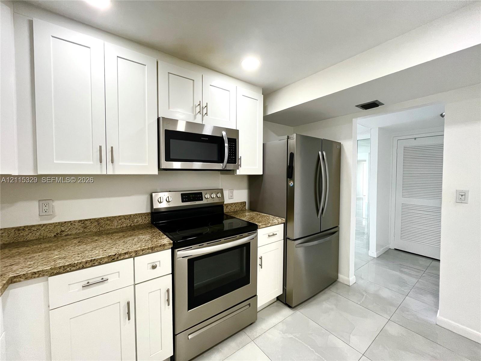 Kitchen featuring white shaker-style cabinetry, stone-finish countertops, stainless steel appliances, and large-format tile flooring